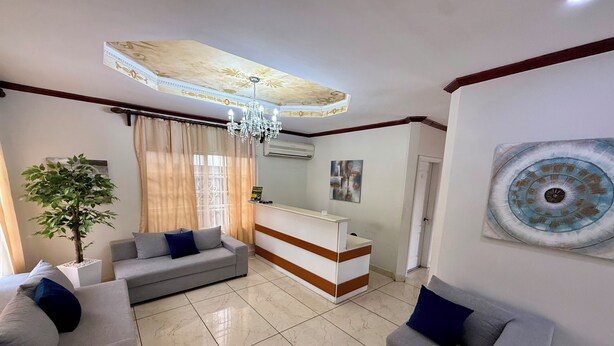 A modern living room with a sofa, a potted plant, a reception desk, and a chandelier.