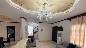 A spacious living area with a chandelier, a sofa, a coffee table, and a staircase leading to an upper floor.