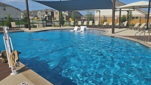 A swimming pool with lounge chairs and umbrellas, surrounded by a fence and buildings.