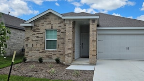 A single-story house with a brick facade, a front garage door, and a small front yard with a concrete pathway.