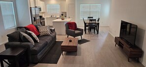 A modern living room with a sofa, coffee table, TV, and dining area.