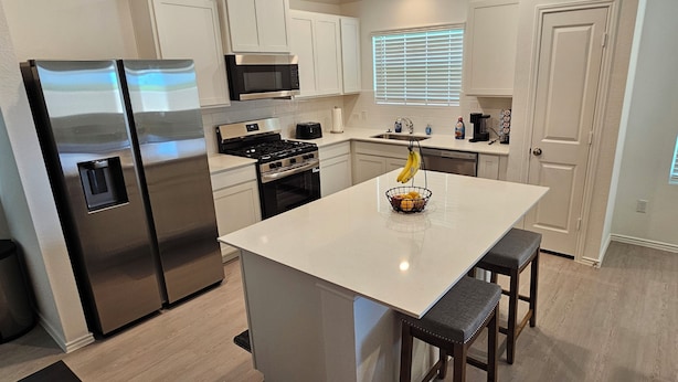 A modern kitchen with stainless steel appliances, a central island with stools, and a window with blinds.