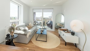 Een moderne woonkamer met een bank, salontafel en een groot raam met uitzicht op gebouwen.