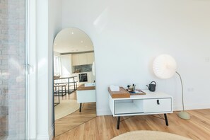 Ein modernes Interieur mit einem weißen Konsolentisch, einer Stehlampe und einem Spiegel, der in die Küche blickt.
