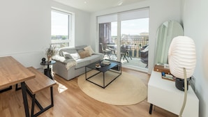Een moderne woonkamer met een bank, salontafel en eettafel, grote ramen en een balkon met tuinmeubilair.