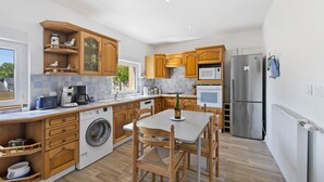 A modern kitchen with wooden cabinets, a built-in washing machine, a dining table with chairs, and a refrigerator. - Gîte Cap with Terrace Near Beaches (Telgruc-sur-Mer)