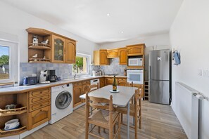 A modern kitchen with wooden cabinets, a built-in washing machine, a dining table with chairs, and a refrigerator. - Gîte Cap with Terrace Near Beaches (Telgruc-sur-Mer)
