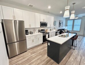 A modern kitchen with white cabinets, stainless steel appliances, a central island, and pendant lighting. - New Modern Luxe 1 Bed 1 Bath w/ Resort Amenities (Waukee)