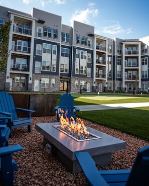Een modern appartementencomplex met meerdere balkons, een vuurplaats met zitplaatsen en een verzorgd gazon.