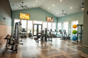 Un gimnasio con equipo de ejercicio, amplias ventanas y ventiladores de techo.