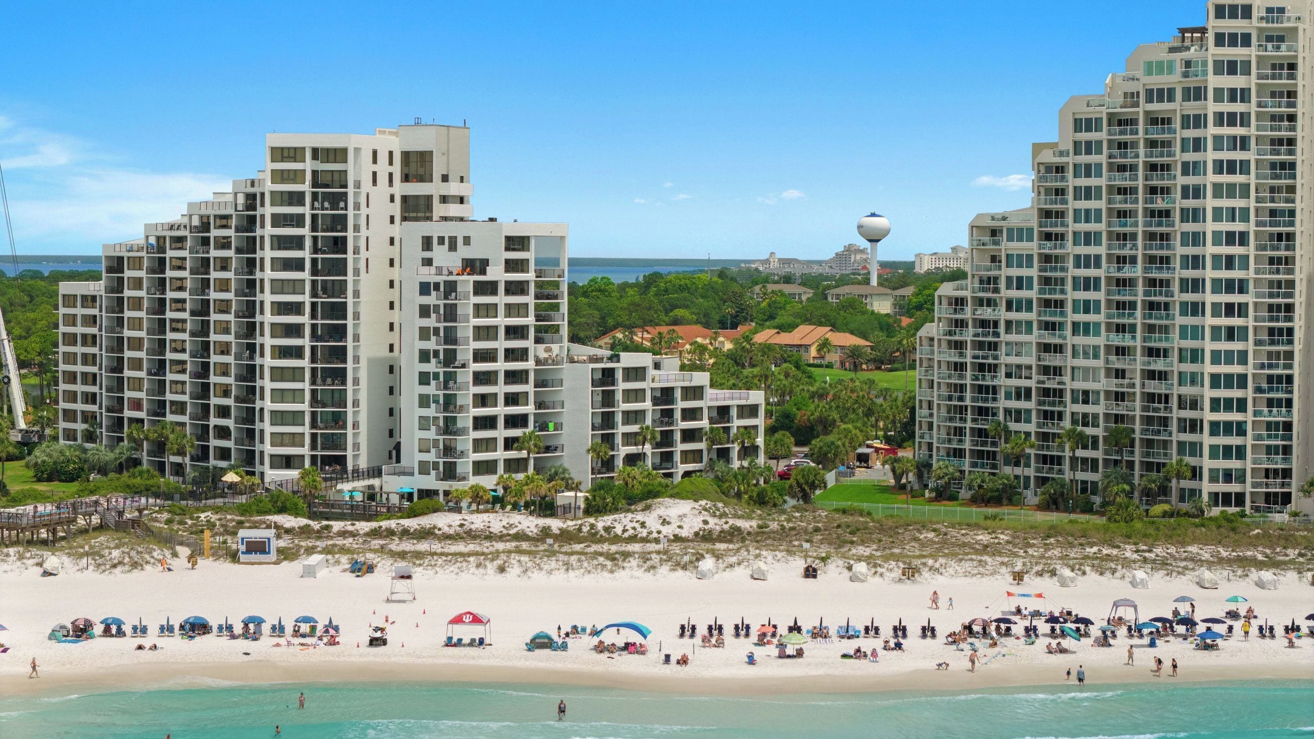Un hotel frente a la playa con varios edificios altos, una playa de arena y una vista despejada del océano.