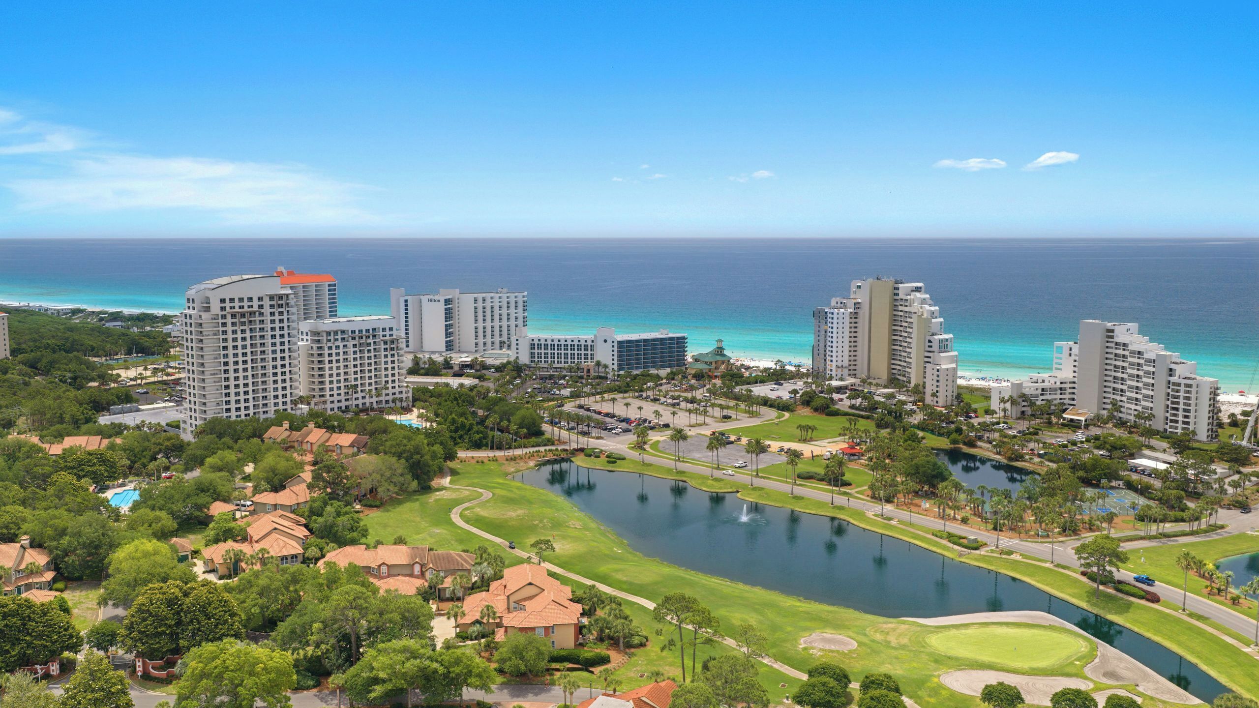 Un complejo hotelero frente al mar con varios edificios altos, un campo de golf y una extensa masa de agua.