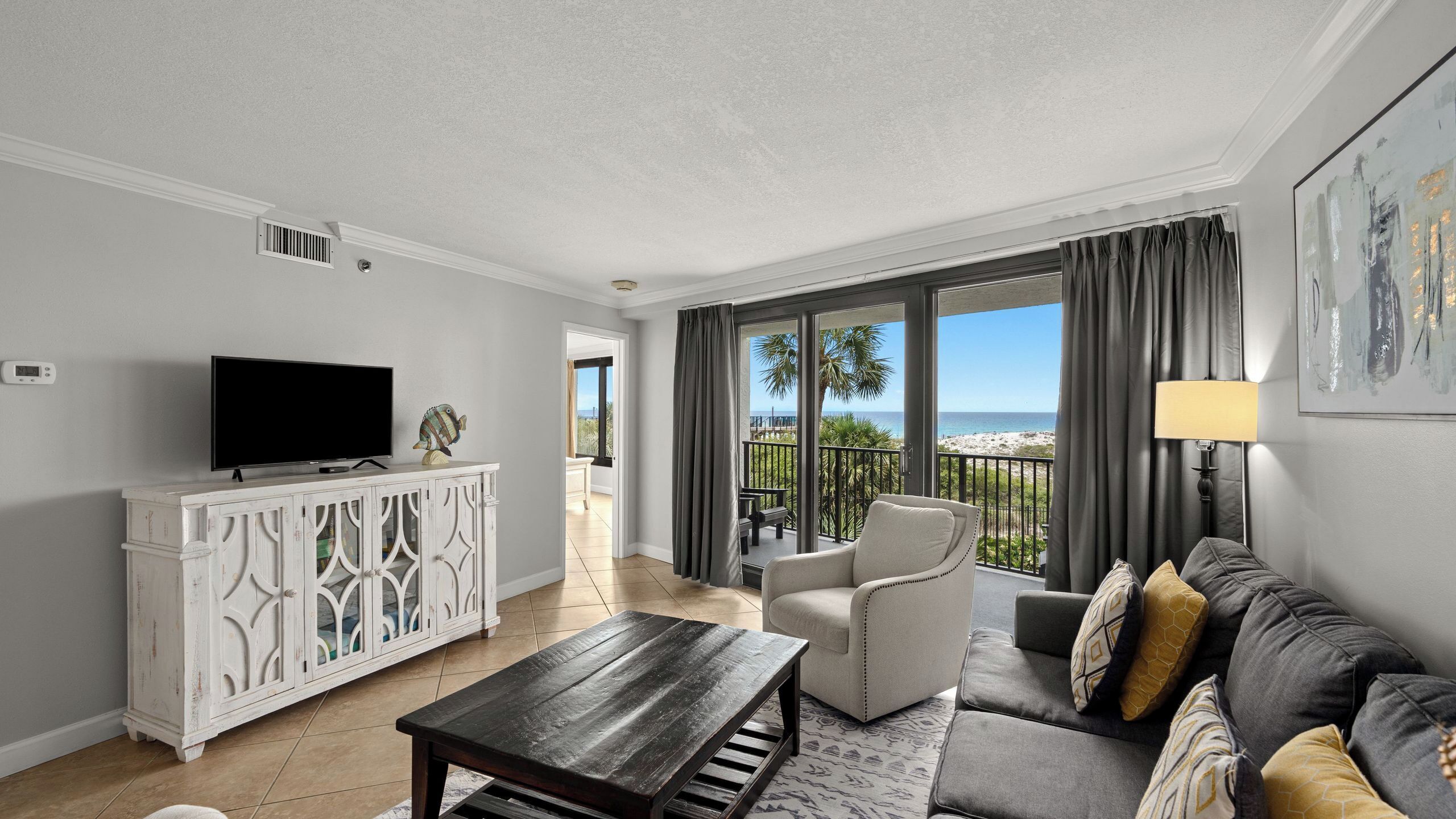 Una sala de estar con televisor, mueble blanco, sofá y un balcón con vistas.