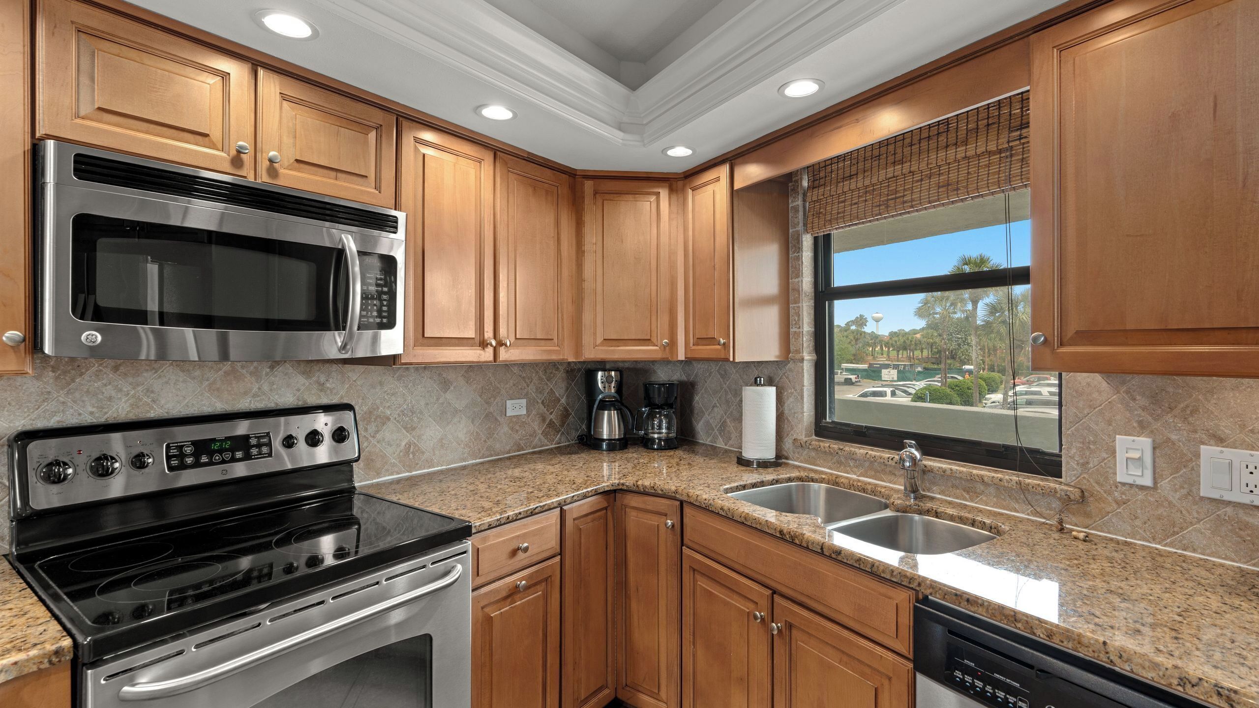 A kitchen with wooden cabinets, stainless steel appliances, granite countertops, a window with a view, and a dishwasher.