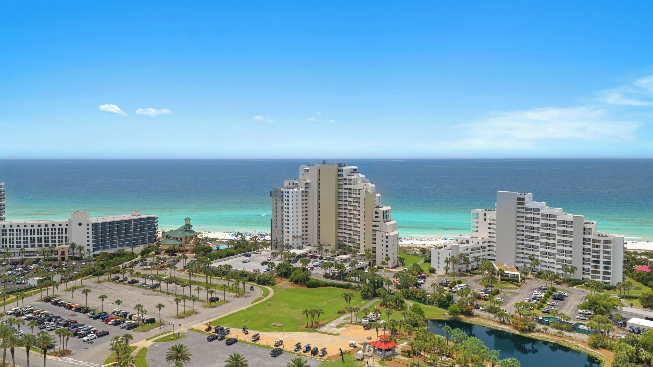 Un hotel costero con varias torres altas, un estacionamiento y vistas a la playa.