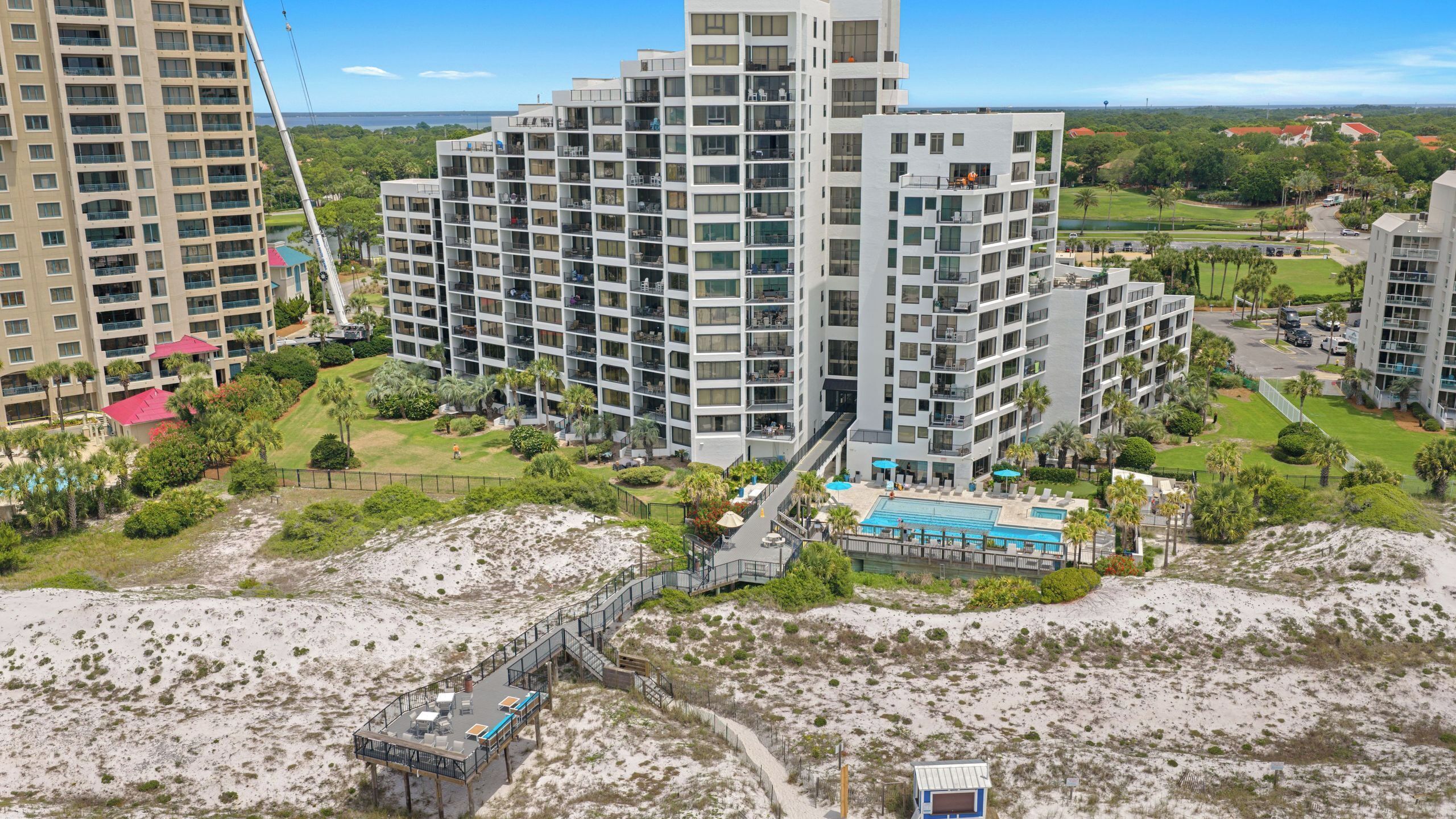 A high-rise hotel with multiple balconies, a pool area, and a beach access walkway.