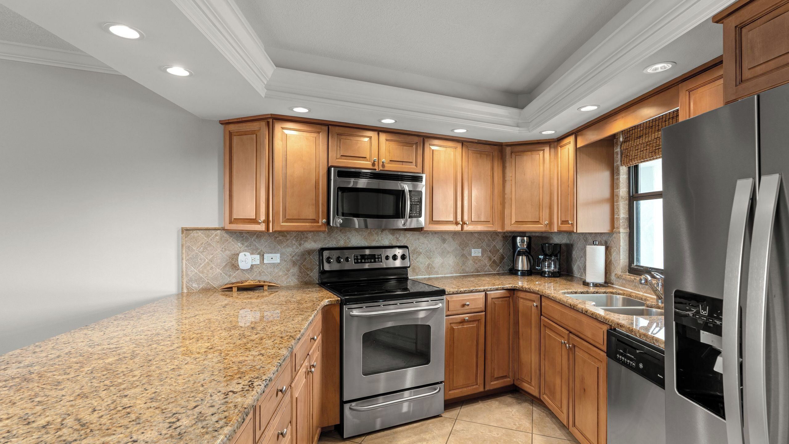 A modern kitchen with granite countertops, stainless steel appliances, wooden cabinets, and a built-in oven.