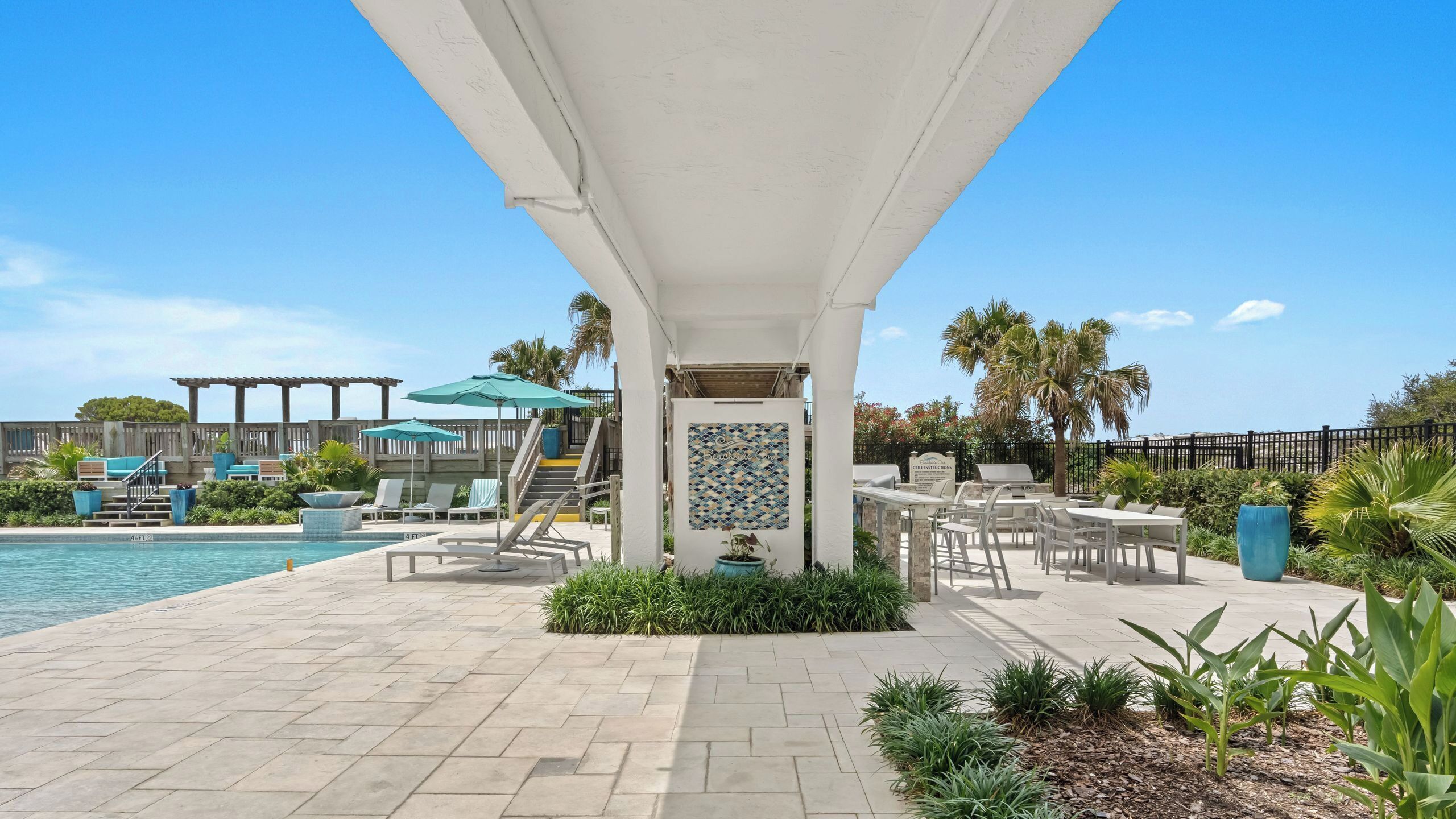 A poolside area with lounge chairs, a covered seating area, and a sign indicating grill instructions.