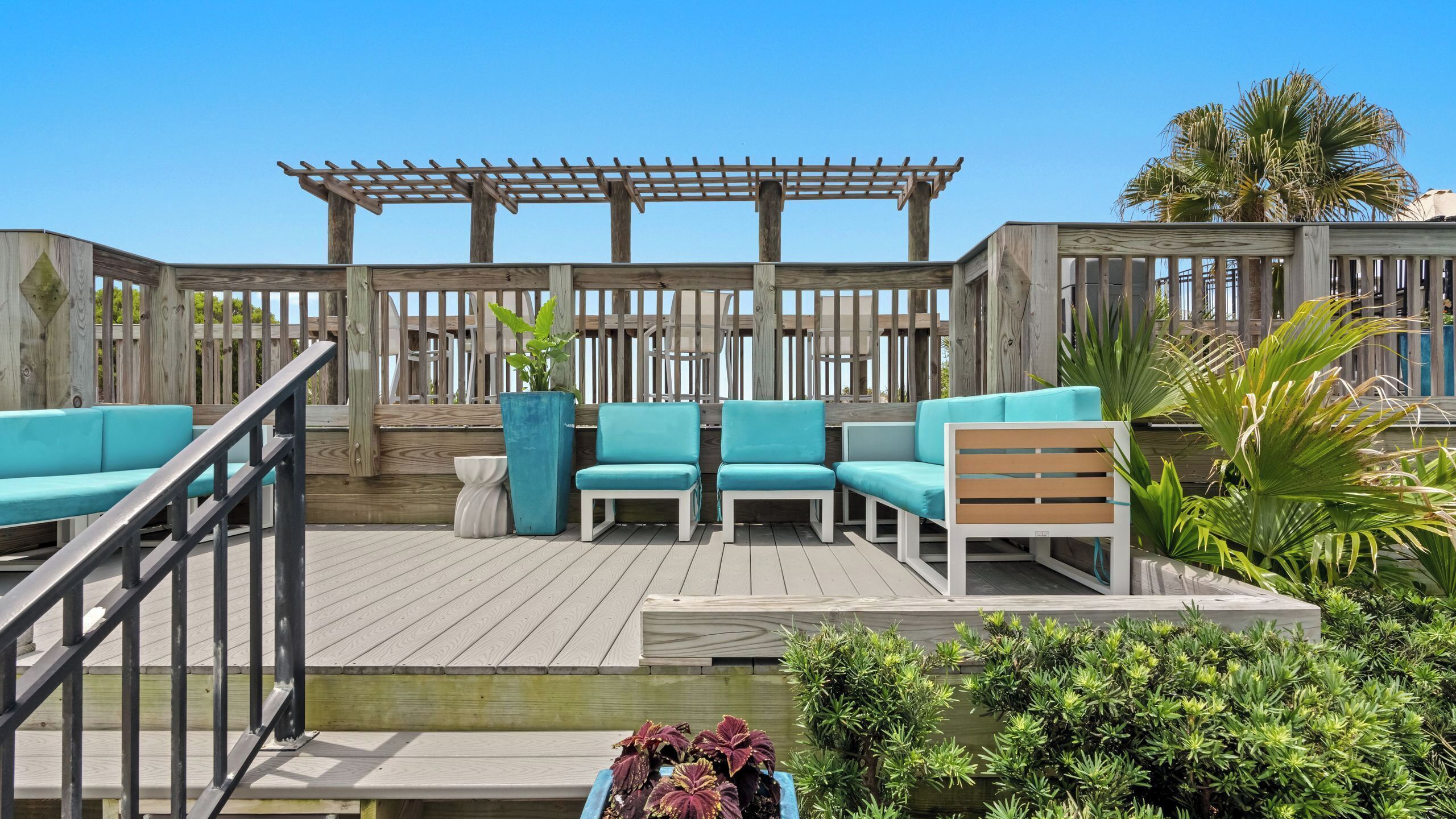 Eine Holzterrasse mit Sitzgelegenheiten im Freien, einer Pergola und Kübelpflanzen.
