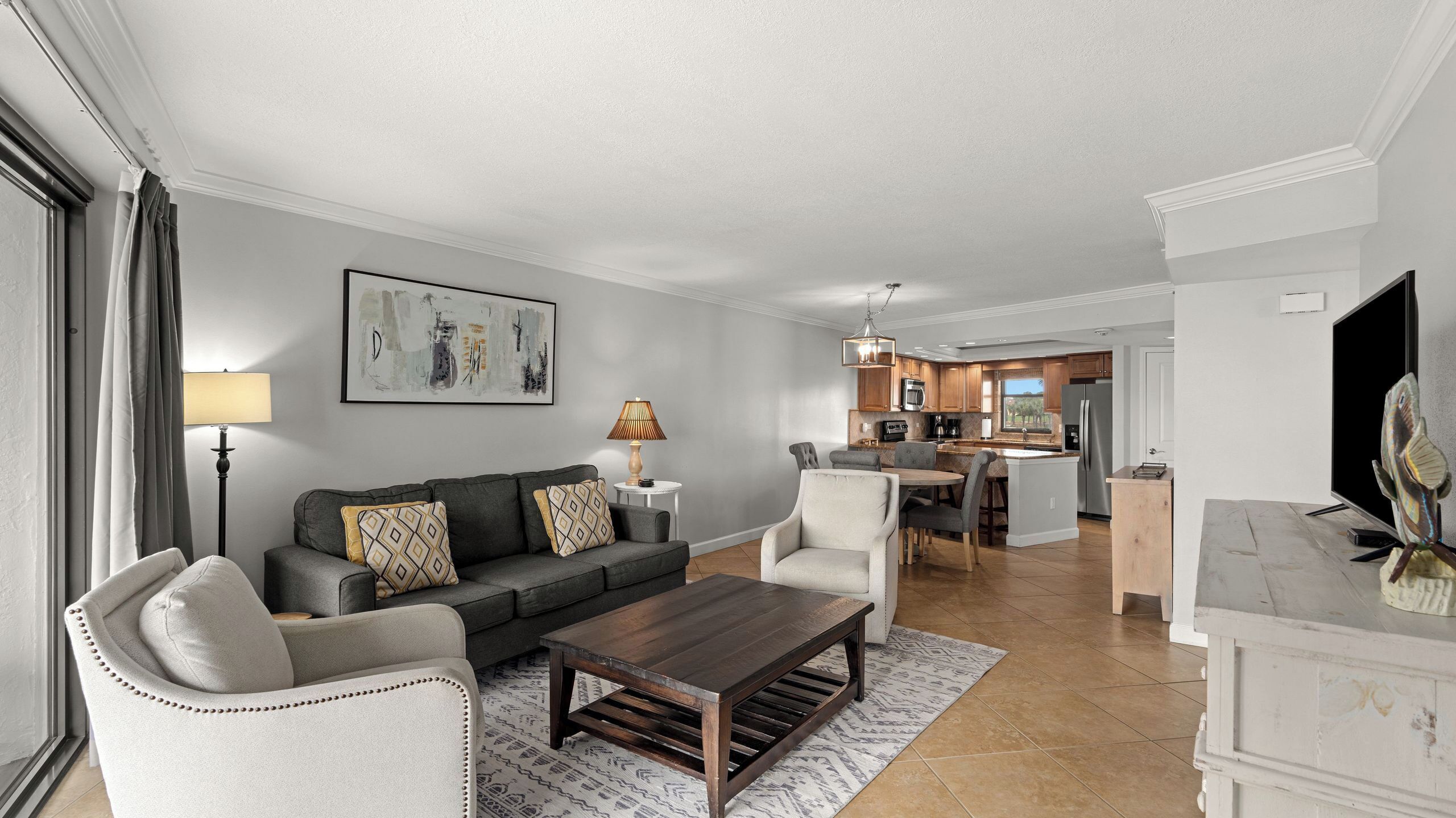 A living room with a sofa, chairs, a coffee table, and a dining area with a kitchen in the background.
