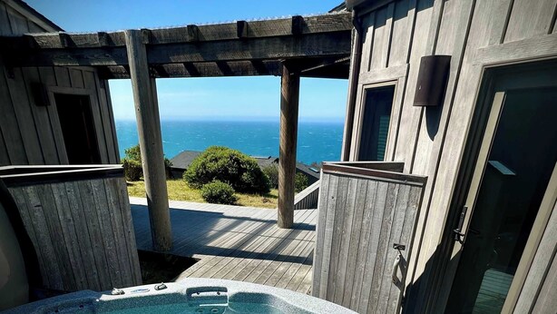 Ein Whirlpool mit einer Holzterrasse, einer Pergola und Blick auf den Ozean.