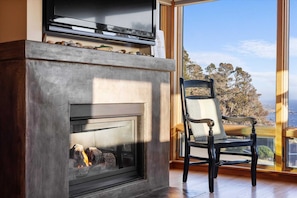 A fireplace with a TV above it, a chair, and a view through a large window.