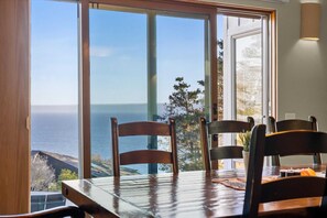 A dining area with a view of the ocean, wooden chairs, and a table.
