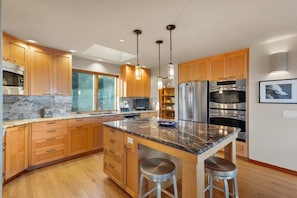 A modern kitchen with wooden cabinets, stainless steel appliances, a marble countertop, and pendant lighting.