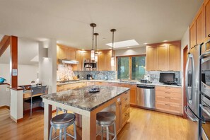 A modern kitchen with granite countertops, stainless steel appliances, wooden cabinets, and a central island with stools.