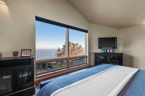 A bedroom with a large window, a bed, a TV on a stand, and a fireplace.