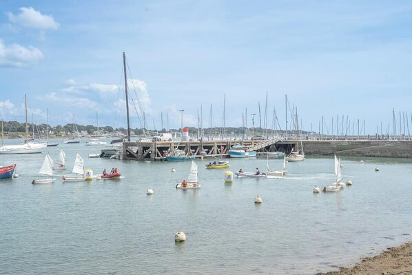 A marina with boats docked, a pier, and a distant shoreline. - La Perle du Port : Vue Panoramique et Terrasse (La Trinité-sur-Mer)