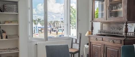 Une pièce avec une grande fenêtre, un meuble en bois, une chaise et un radiateur.