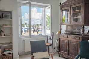 A room with a large window, a wooden cabinet, a chair, and a radiator. - La Perle du Port : Vue Panoramique et Terrasse (La Trinité-sur-Mer)