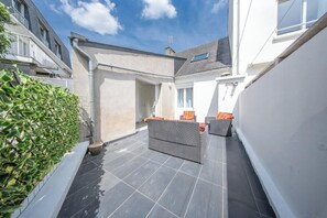 A courtyard with a wicker sofa, a potted plant, and a tiled floor. - La Perle du Port : Vue Panoramique et Terrasse (La Trinité-sur-Mer)