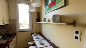 Een keuken met een lange toonbank, krukken, een raam en een kleurrijk abstract schilderij.
