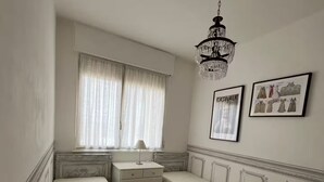 Een slaapkamer met twee bedden, een dressoir, een stoel, een kroonluchter en twee foto's in lijsten aan de muur.