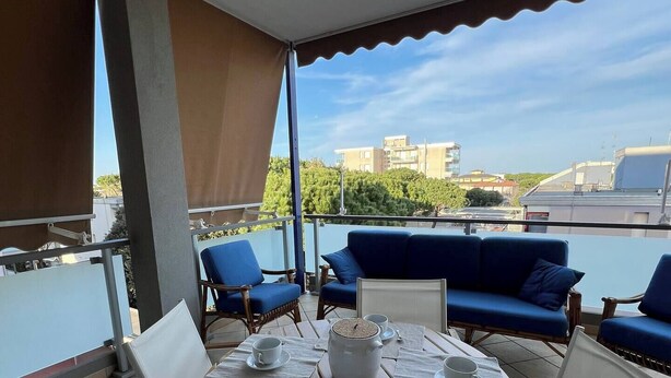 Een terras met een tafel gedekt voor twee, blauwe banken en uitzicht op gebouwen en groen.