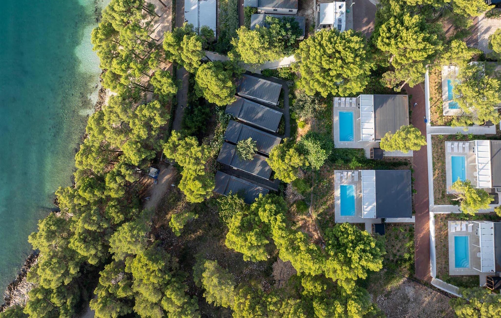 An aerial view of a coastal property with multiple buildings, a swimming pool, and dense greenery.