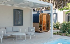 Ein moderner Außenbereich mit Pool, einer Holzsauna und einer überdachten Terrasse.