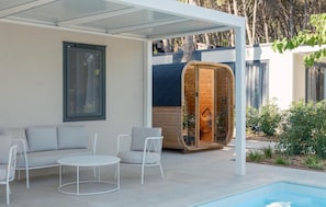 Ein moderner Außenbereich mit Pool, einer Holzsauna und einer überdachten Terrasse.