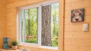 En stuga med träpanel på insidan, med en köksbänk, två barstolar, ett fönster med utsikt över träd och en tavla på väggen.
