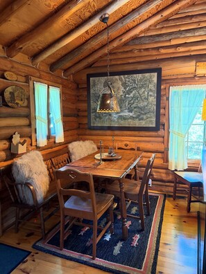 A rustic wooden cabin interior with a dining table, chairs, a hanging lantern, and a framed picture on the wall. - Dancing Bear Cabin: Authentic storybook log cabin with Lake Michigan views (Harbor Springs)