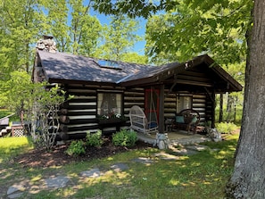 A log cabin with a porch, a swing chair, and a stone fireplace.
