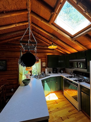 A rustic kitchen with wooden beams, a large window, and a hanging pot rack.