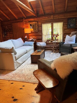 A cozy log cabin interior with a sofa, armchair, and a small wooden table.
