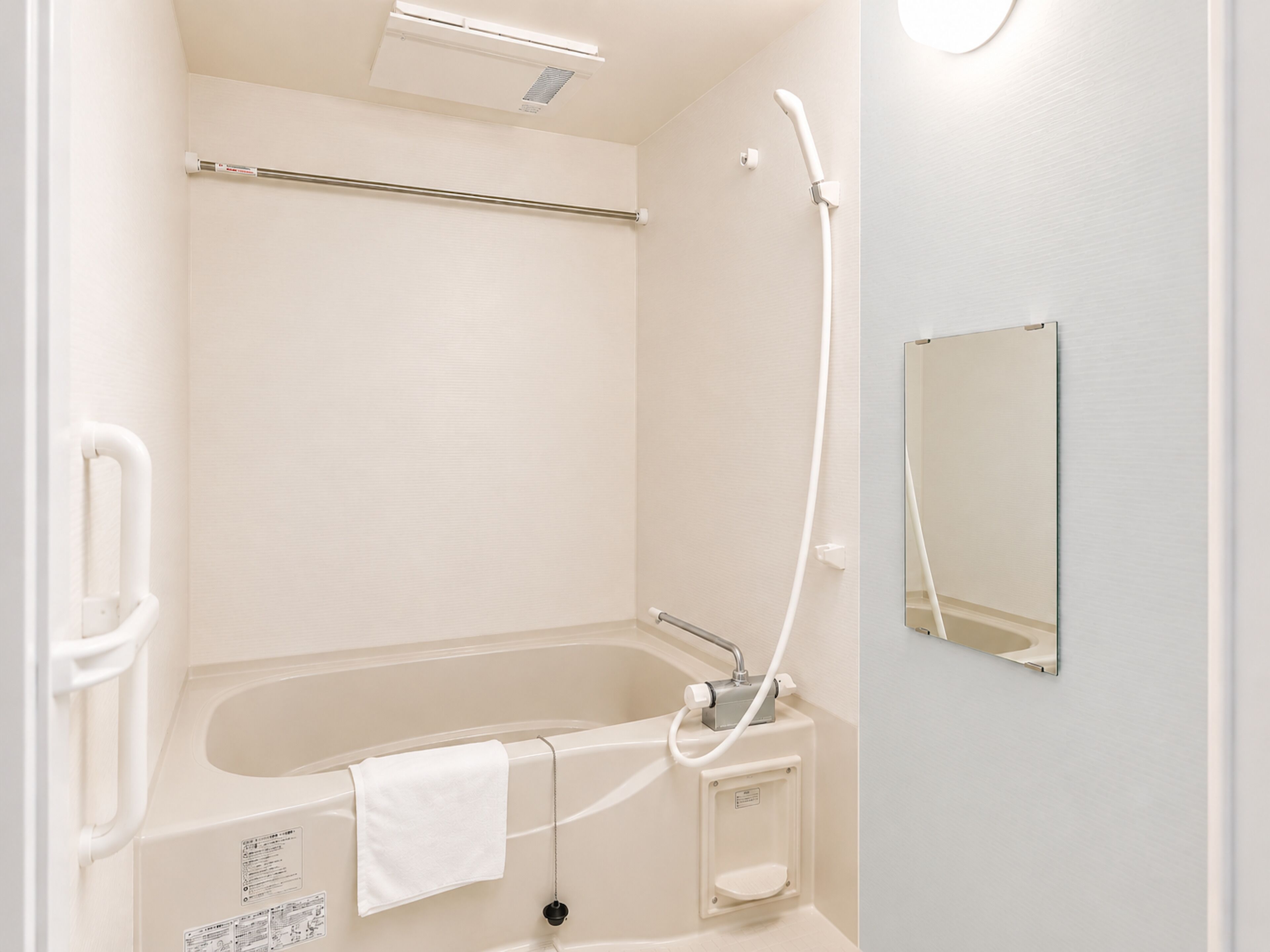 A bathroom with a bathtub, a handheld showerhead, a towel, and a mirror.