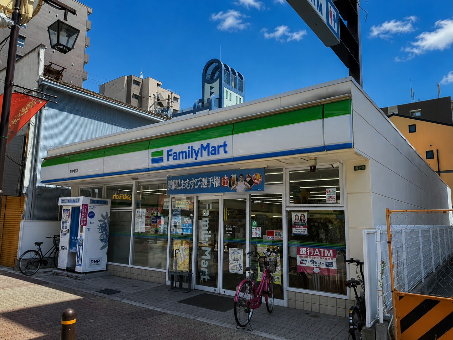 Una tienda FamilyMart con entrada despejada, una bicicleta estacionada afuera y un letrero visible de cajero automático.