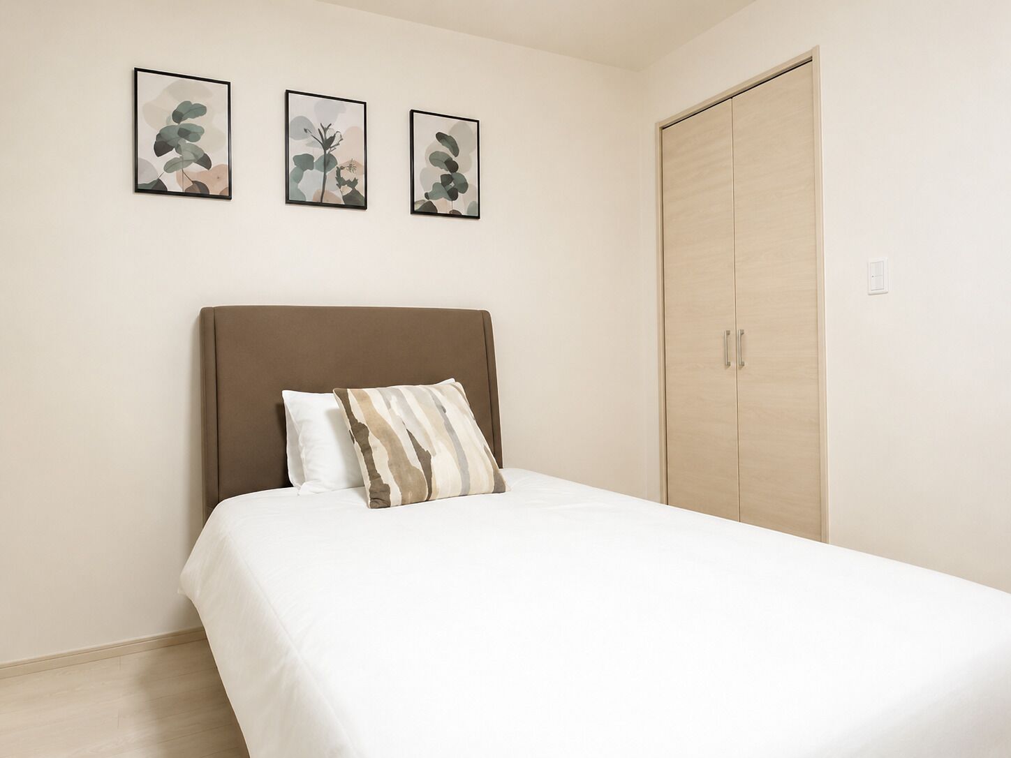 A bedroom with a bed, a wardrobe, and three framed artworks on the wall.