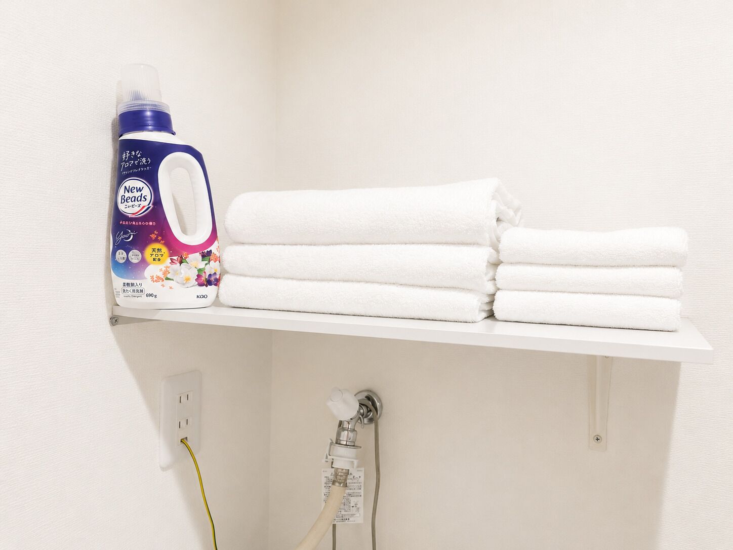 A bathroom shelf with a bottle of New Beads laundry detergent and neatly folded white towels.