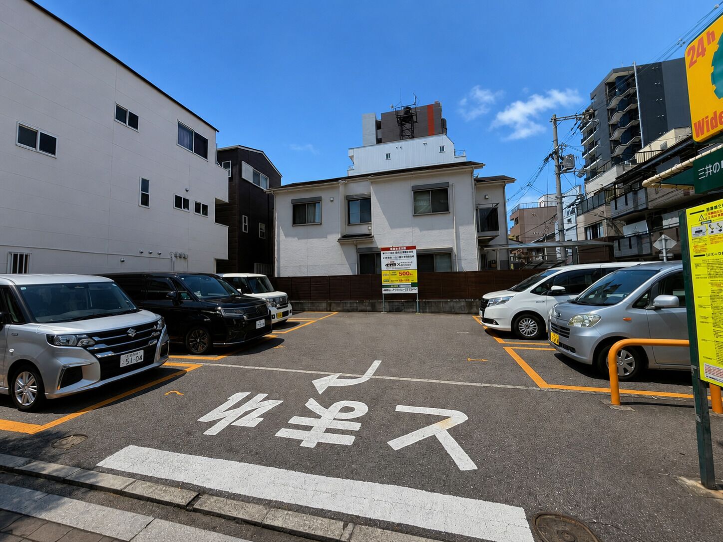 Un parking rempli de voitures, un bâtiment avec une enseigne et un ciel dégagé.